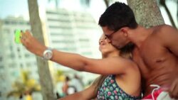 Young Brazilian couple take selfie and kiss under palm tree on Rio beach Stock Footage