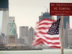 The Statue of Liberty with the Freedom tower behind a flag waves from a pole that says "No Trespassing, No Dumping" Stock Footage
