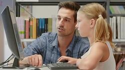 DS Man helping girl learn to use computer in library Stock Footage