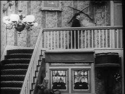 B/W 1916 Charlie Chaplin walking into swinging clock pendulum + falling down stairs / AUDIO Stock Footage