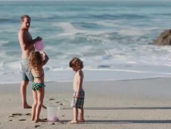 MS R/F TU Boy and girl walk over container of water balloons and man blows balloons while kids pick them up out of container on beach / Montezuma, Puntarenas, Costa Rica Stock Footage