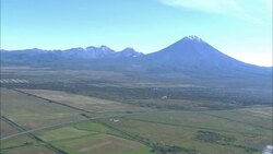Volcanic mountains border green fields. Stock Footage
