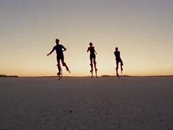 Low angle long shot woman and two men running in desert on skyrunners towards CAM with sunset in background Stock Footage