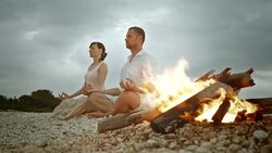 PAN Couple doing half lotus on beach by the fire Stock Footage