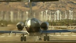 American Airlines passenger jet enters runway and accelerates for takeoff spewing thick clouds of hot jet exhaust fumes and gases being pumped out of jet engines against background of windfarm Stock Footage