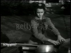 1941: WWII HOME FRONT: Girl Scout 'Carol Davis' dumping collected tin foil. 'Carol' placing aluminum pots, pans in car, scrap, recycling. Girl Scouts placing books, board games into car. 'Carol' putting up 'Young America Wants to Help' poster. Instructional Video