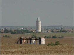 MS grain elevator and oil storage tanks amidst golden wheat fields, zoom out to WA, prairie horizon, Heat haze, USA Stock Footage