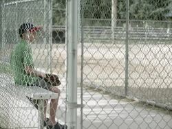 Slow motion push of boy sitting in dugout behind chain link fence. Stock Footage
