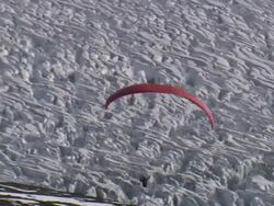 Wide Shot aerial - The wing of a paraglider billows up over a cliff as a pilot steps off the edge and sails over a snowy valley / Alaska, USA Stock Footage