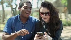 Friends point and laugh at smartphone and take selfie together outside in public park Stock Footage
