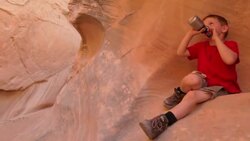 Young hiker boy rests on red-rocked canyon wall while drinking water bottle Stock Footage