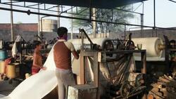 A boy and a man feed dyed fabric into a machine to be washed and rolled in a garment factory. Stock Footage