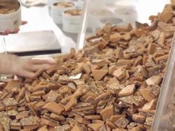 CU TU confectionary worker selects toffee pieces from large pile of freshly made almond toffee bark and fills tin can container with toffee  / Rancho Mirage, California, USA Stock Footage