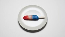 'A red, white and blue ice pop melts on a white plate.' Stock Footage