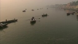 Rowboats approach the ghat where men perform ablutions at the foot of a temple on the Ganges River. Stock Footage