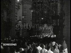 1943: MEXICO RELIGION: MS Mexican women carrying children on street. WS Mexicans entering church. INT WS Religious ceremony, altar, priest. WS Mexicans praying. MS Woman on their knees at altar. MS Woman, arms spread, praying. MS Mexican men, praying. Instructional Video