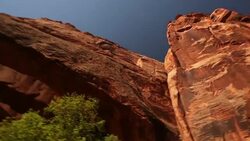 Sun shines down on rocky mountains and red-rock mountain arch in the desert in Utah (pan) Stock Footage