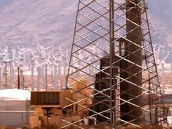 PAN follows freight train pulling double stacked containers through California desert against background of 1000 windmills of wind farm and natural gas powered plant in foreground  / Palm Springs, California, USA Stock Footage