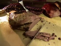 Medium Close Up hand-held pan-right zoom-in zoom-out - A cook prepares a brisket sandwich near barbecue ribs on a restaurant counter. / Dallas, Texas, USA Stock Footage