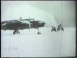 1943: ALEUTIAN ISLANDS CAMPAIGN: UNITED STATES ARMY: VS Snow plow plowing snow on U.S. Navy airfield base in Amchitka, Alaska, Douglas B-18 Bolo medium bomber aircraft (L) frame, soldiers sweeping snow off wing of bomber. WWII, Pacific Front Instructional Video