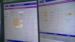 A technician watches two computer screens and a security monitor at a work table. Stock Footage