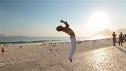 Capoeira martial artist cartwheels and flips backwards across sunny Brazilian beach boardwalk Stock Footage