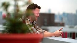 Hip young man on Brooklyn rooftop laughs at funny text-message (dolly-shot) Stock Footage
