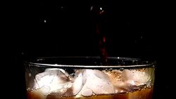 Pouring cola soda into glass of ice with splashes at slow motion on black background Stock Footage
