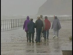 MS Group of people (some disabled) walking along sea front during storm, away from camera Stock Footage