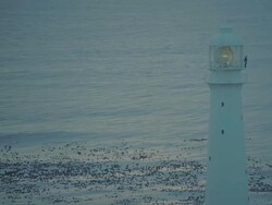 WS AERIAL View of Lighthouse light turning round at sunset sunrise with keeper standing on platform Stock Footage
