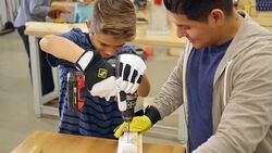 Hispanic father or instructor at woodworking day camp for kids teaches student or son to drill screw into boards Stock Footage