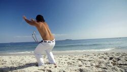Sand flies as capoeira martial artist somersaults backwards across Brazilian beach in slow motion Stock Footage