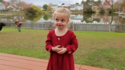 Young girl innocently sings as her older brother chases the family dog around the backyard behind her Stock Footage