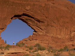 Many people standing and sitting within a massive sandstone arch called North Window in the spectacles area Stock Footage