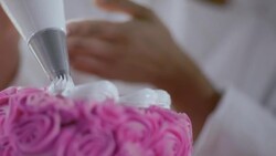 Pastry chef decorates pink cake with white icing designs Stock Footage