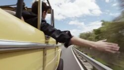 Young man riding in passenger seat of classic Bronco holds hand out the window, laughs with friends, and points at passing scenery Stock Footage