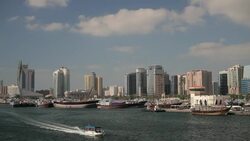 A ferryboat sails past commercial vessels docked along the port at Deira, Dubai. Stock Footage