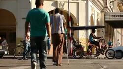 LS of Cuban Man with Crutches & Pedestrians crossing Havana street Stock Footage