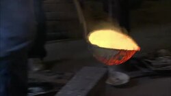 A metal caster uses a ladle to pour molten metal into a furnace at a foundry. Stock Footage