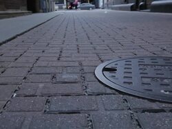 CU of permeable alleyway with manhole cover, traffic in background Stock Footage