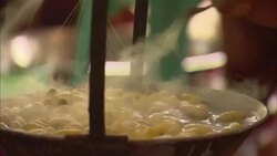 Steam rises from a kettle of silk cocoons while a woman stirs. Stock Footage