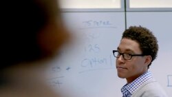 Hip young businessman writes on white-board, instructs office conference-room Stock Footage