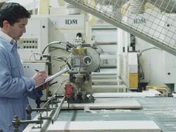 worker holding clipboard checking panes of fiberboard as they enter a processing machine in a furniture factory Stock Footage