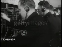 1938: NYPD: EXT Police Department building. INT Building: Men working switchboard. Policeman sticking papers on spindle. CU Teletype machine typing Missing Persons bulletin. Papers being handed to Dispatcher. Precinct 7 Police car on street. Instructional Video