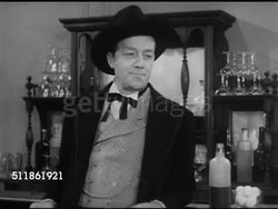 1952: 19th CENTURY GAMBLER: 'Jack O'Diamonds' drinking whiskey at bar, watching men playing poker at table.  VO 'Jack O'Diamonds': Johnny taking chance out by dealing a round of studs. Instructional Video