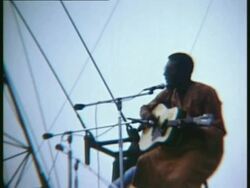 1969 MONTAGE LA MS Richie Havens standing on stage, singing and playing guitar at Woodstock music festival/ Bethel, New York, USA Stock Footage