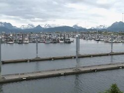 "Wide view of boats in Homer Boat Harbor, snow capped mountains of Kachemak Bay State Park and Wilderness Park in background, Homer Spit, Homer, Kenai Peninsula, Alaska." Stock Footage