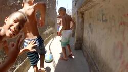 Young Brazilian boys kick soccer ball through crumbling stone alley, smile and make peace signs at camera Stock Footage