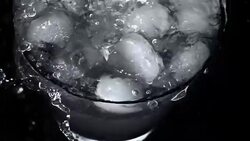 Pouring water into glass of ice with splashes at slow motion on black background Stock Footage