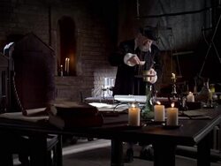 Nostradamus stands in a candlelit room, pours an ingredient into a bowl, and begins stirring. Stock Footage